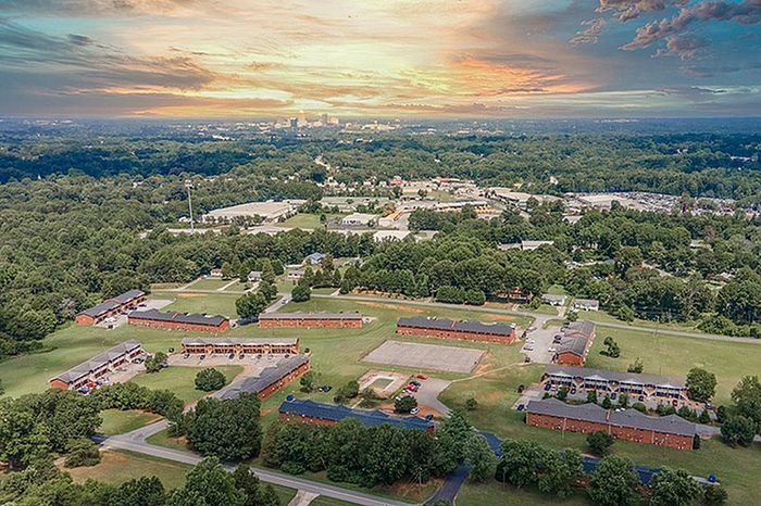 Breathtaking aerial view of a peaceful residential community surrounded by lush greenery, under a vibrant sunset sky.