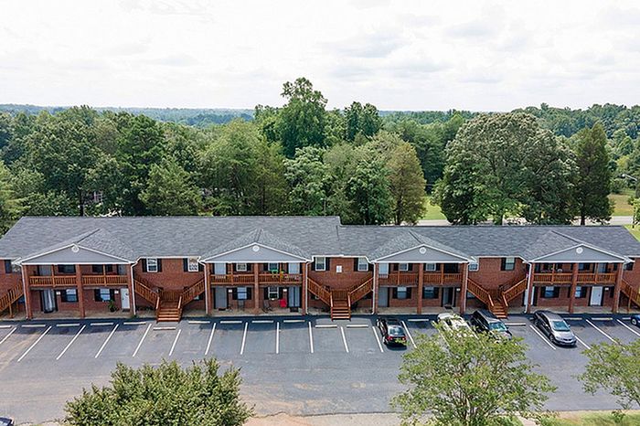 Charming brick apartment complex set amid lush greenery, featuring convenient parking and inviting balconies.