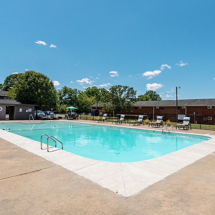 Inviting community pool area with clear blue water, surrounded by sun loungers and lush greenery, perfect for a relaxing summer day.