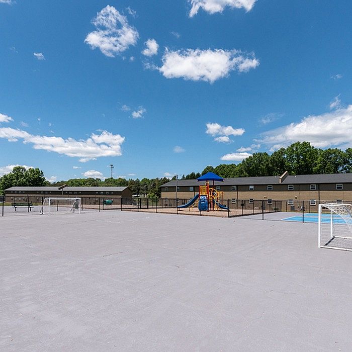Sunlit outdoor playground and sports court in a serene residential community, surrounded by lush greenery and modern buildings.