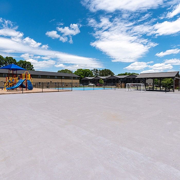 Vibrant apartment community with a spacious outdoor playground, inviting swimming pool, and covered seating area, set against a clear blue sky.