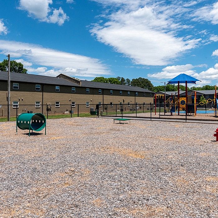 Vibrant community playground with modern play structures, surrounded by a spacious open area and residential buildings under a bright blue sky.