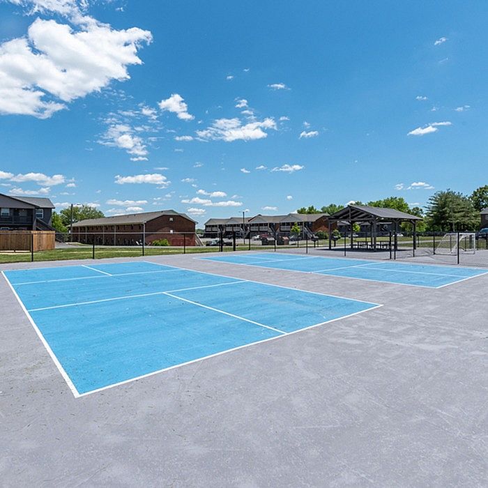 Vibrant outdoor sports courts under a clear blue sky, surrounded by lush greenery and modern apartment buildings.