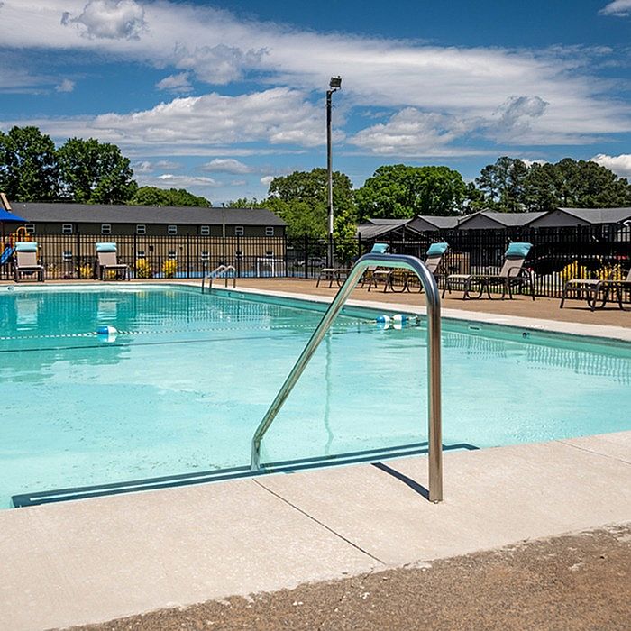 Inviting outdoor pool area with crystal-clear water, surrounded by lush green trees and comfortable lounge chairs, perfect for relaxation.