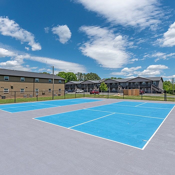 Inviting apartment complex featuring a vibrant tennis court under a clear blue sky, perfect for active outdoor living.