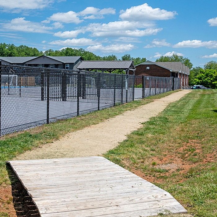 Inviting pathway leading to a sunny recreational area with sports facilities, surrounded by lush greenery and charming residential buildings.