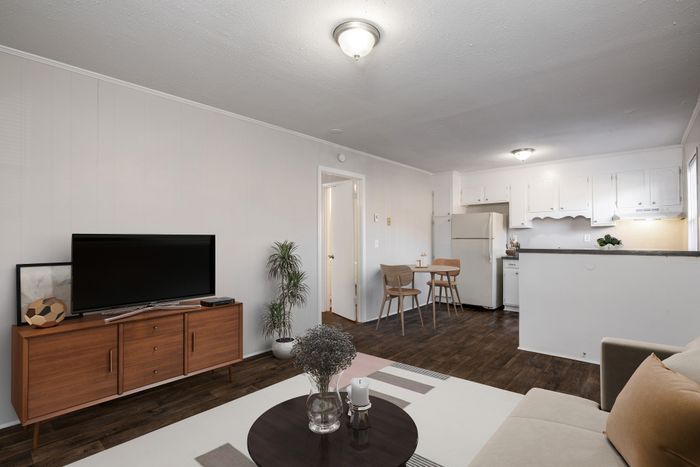 Modern open-concept living room and kitchen with sleek wooden floors, stylish furniture, and abundant natural light.