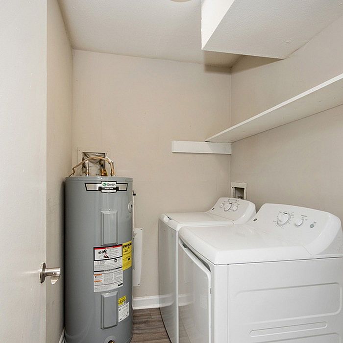 Modern laundry room featuring a sleek washer and dryer set next to a compact water heater, with convenient shelving for storage.