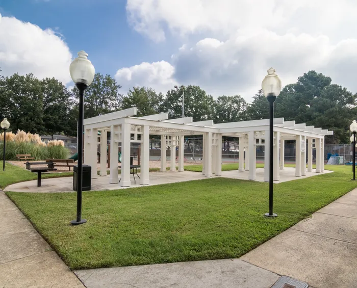 Charming outdoor community area with a modern pergola, surrounded by lush greenery and stylish lamp posts.