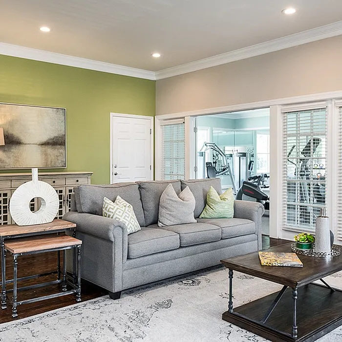 Chic living room with a cozy grey sofa, stylish decor, and modern fitness room view creating a harmonious blend of comfort and functionality.