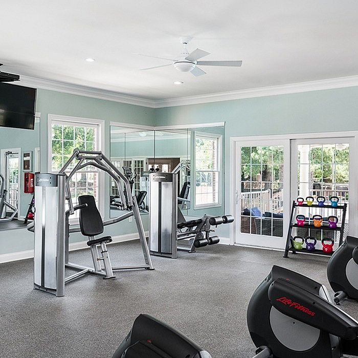 Bright and spacious fitness room with modern gym equipment, large mirrors, and natural light from the windows.