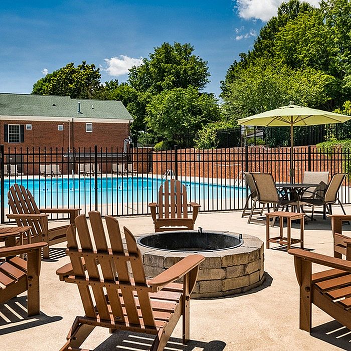 Inviting outdoor space with Adirondack chairs surrounding a cozy fire pit, overlooking a refreshing pool and lush green surroundings.