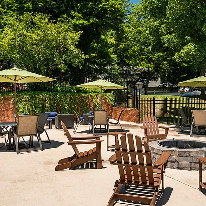 Inviting outdoor patio with wooden chairs and tables under vibrant green umbrellas, perfect for relaxation and social gatherings in a lush garden setting.