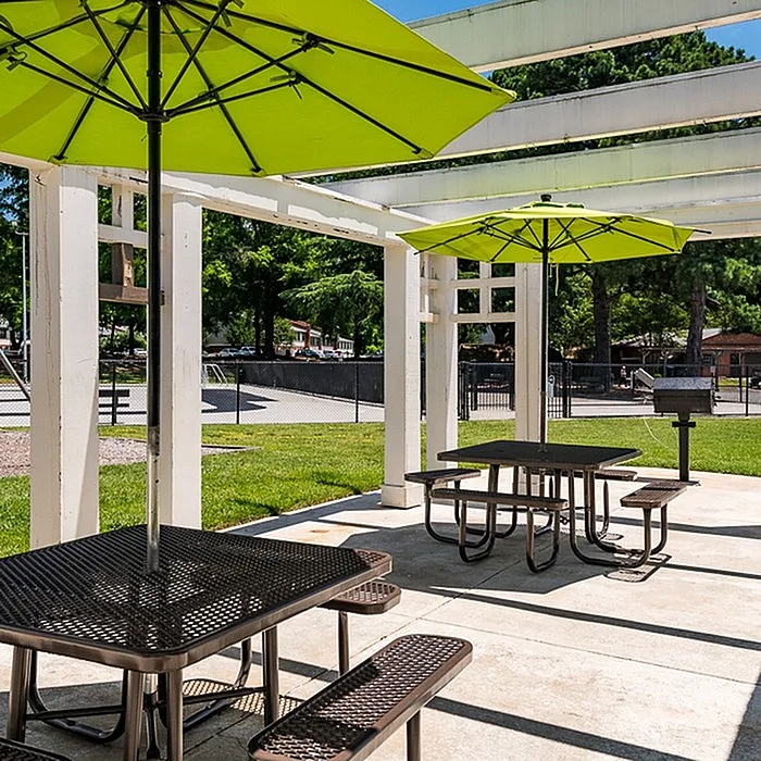 Inviting outdoor area with picnic tables under vibrant green umbrellas, perfect for gatherings and barbecues.