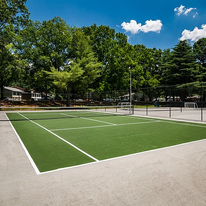 Inviting outdoor tennis court surrounded by lush greenery and clear blue skies, ideal for recreational sports and fitness enthusiasts.