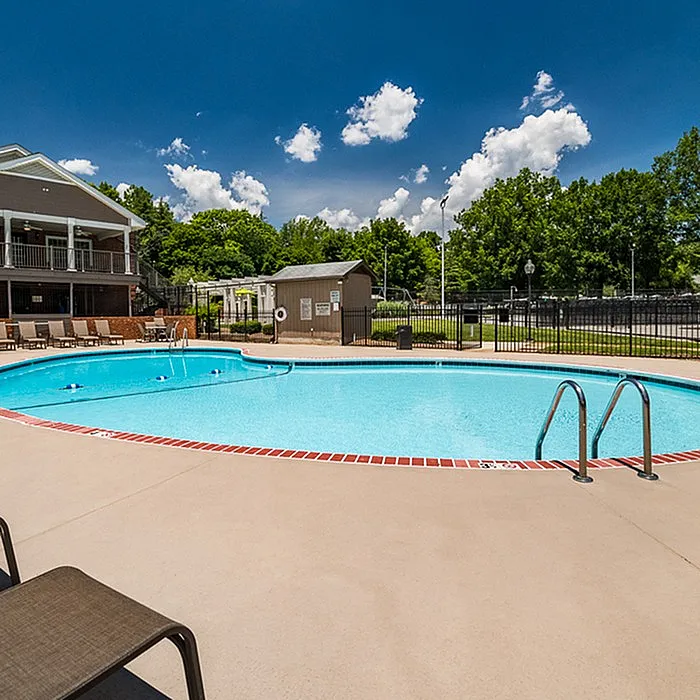 Inviting outdoor pool area with crystal-clear water, surrounded by lush greenery and lounge chairs under a bright blue sky.