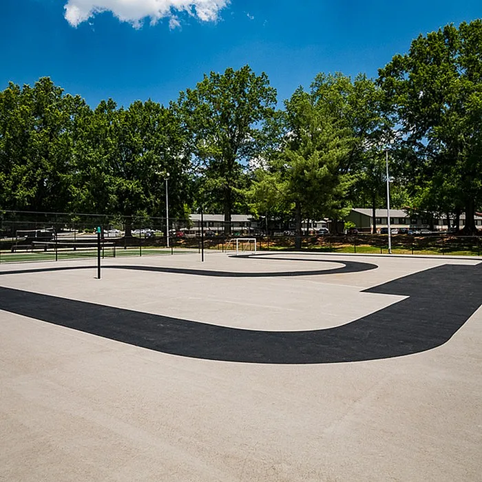 Spacious outdoor recreational area featuring a modern skate track surrounded by lush green trees under a vibrant blue sky.