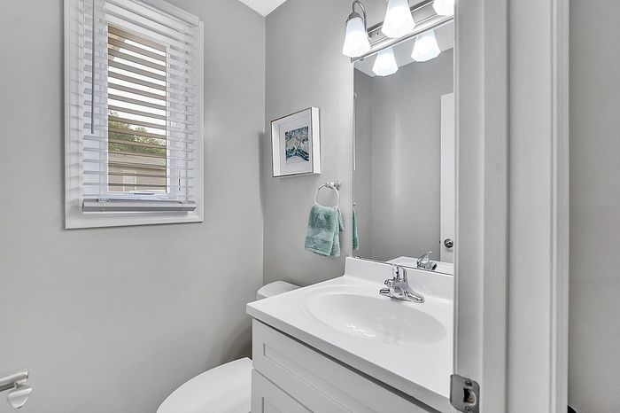 Modern bathroom with sleek white vanity, polished fixtures, and natural light streaming through a window with blinds.