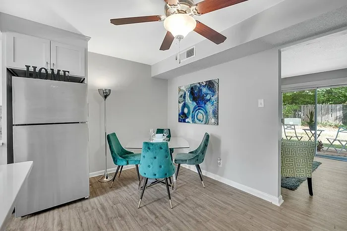 Chic dining area with vibrant teal chairs, modern art, and natural light from sliding doors leading to a charming patio.
