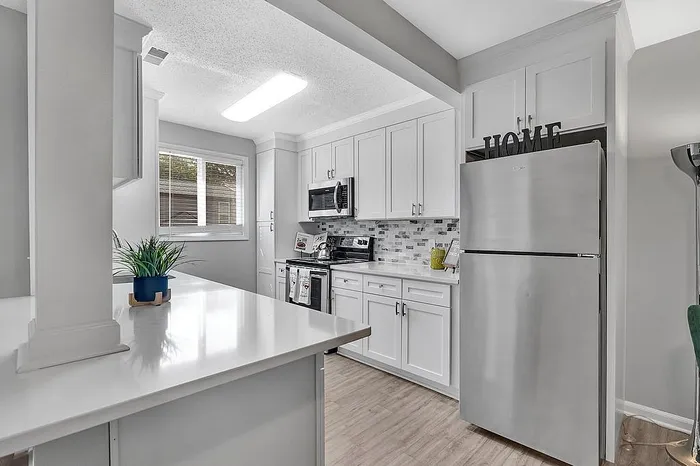 Modern kitchen with sleek stainless steel appliances, elegant white cabinetry, and stylish tile backsplash, offering a bright and inviting atmosphere.