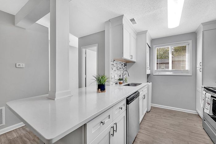 Chic kitchen with modern white cabinetry, elegant countertops, stainless steel appliances, and natural light streaming through a large window.