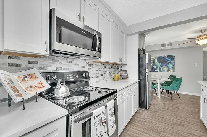 Modern kitchen with sleek stainless steel appliances, elegant white cabinetry, stylish backsplash, and an inviting adjacent dining area with vibrant green chairs.