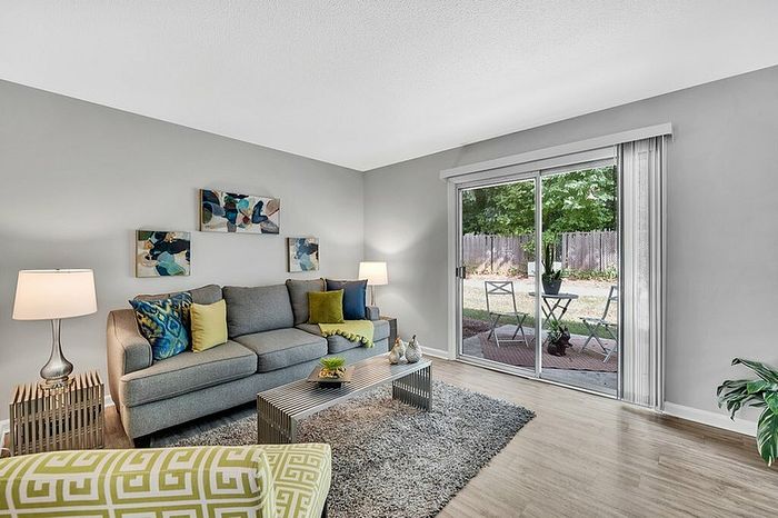 Inviting living room with stylish decor, featuring a cozy gray sofa, vibrant cushions, and a large glass door opening to a charming patio.