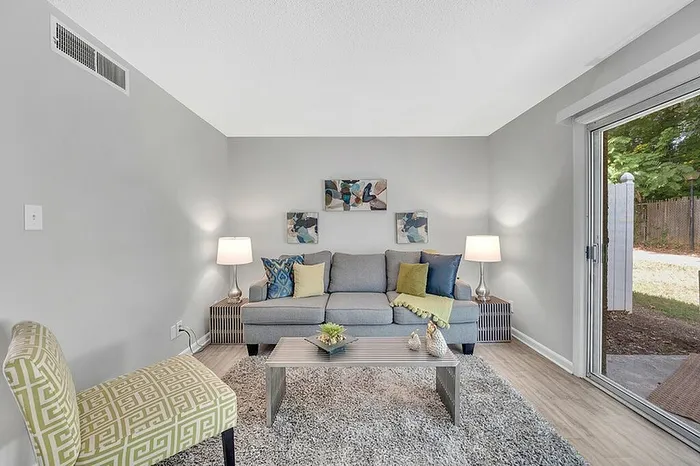 Bright and inviting living room featuring a contemporary gray sofa, decorative pillows, and stylish lamps. Large sliding glass doors open to a serene outdoor space, enhancing natural light and tranquility.
