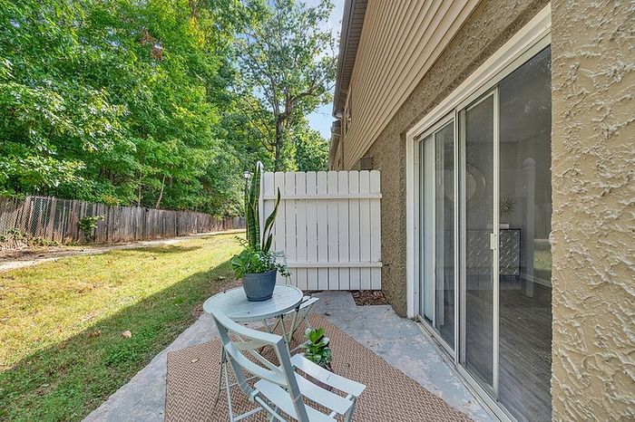 Charming outdoor patio with lush greenery, featuring a cozy seating area and elegant sliding glass doors for seamless indoor-outdoor living.
