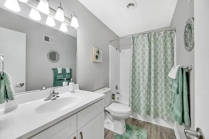 Elegant bathroom featuring a sleek white vanity, modern fixtures, and a soothing green color theme with patterned shower curtain and matching towels.