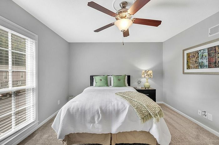 Inviting bedroom with plush bed, stylish decor, and natural light from large window, perfect for relaxation.