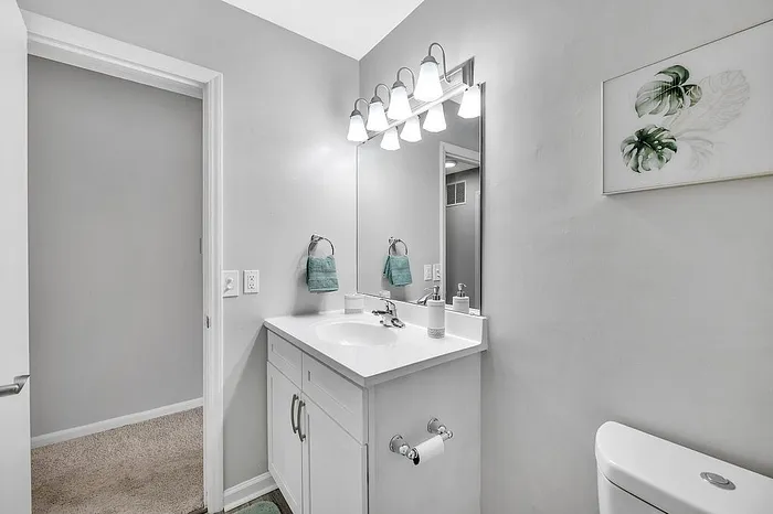 Elegant bathroom with modern white vanity, stylish lighting fixtures, and calming green accents, creating a serene ambiance.