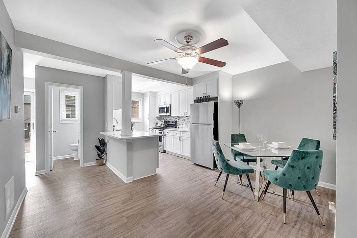 Modern apartment with open-concept kitchen and dining area featuring stylish teal chairs and elegant lighting.