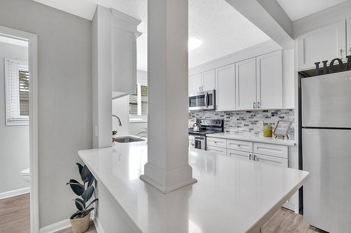 Bright, modern kitchen featuring sleek white cabinets, stylish tiled backsplash, and stainless steel appliances, creating a welcoming cooking space.
