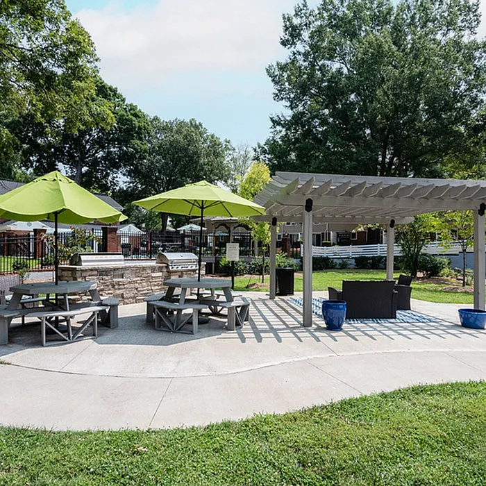 Inviting outdoor space featuring shaded picnic tables, modern pergola, and vibrant green umbrellas in a serene park-like setting.
