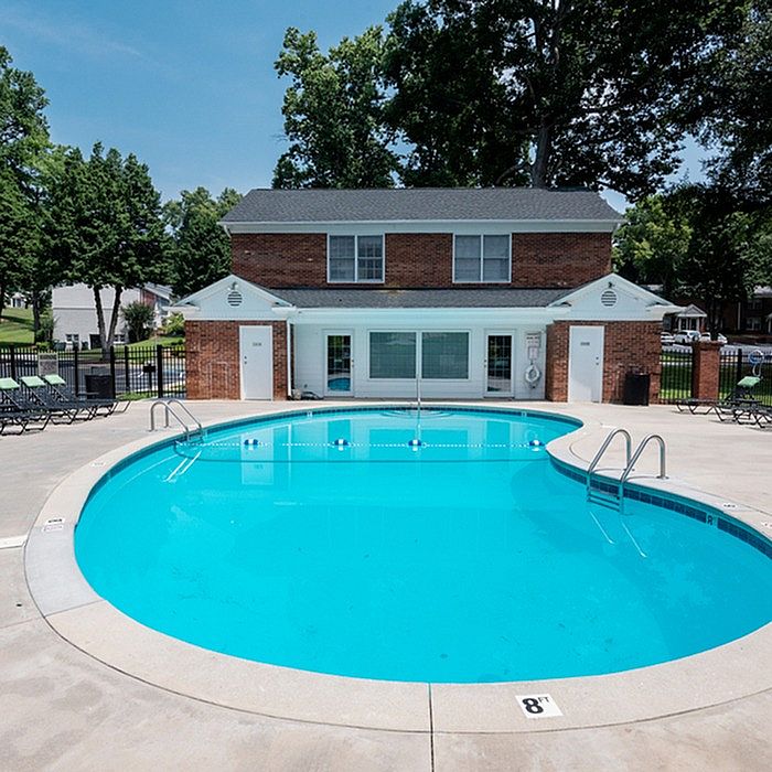 Inviting outdoor pool area with clear blue water, surrounded by lush greenery and a charming brick clubhouse, perfect for relaxation and leisure.