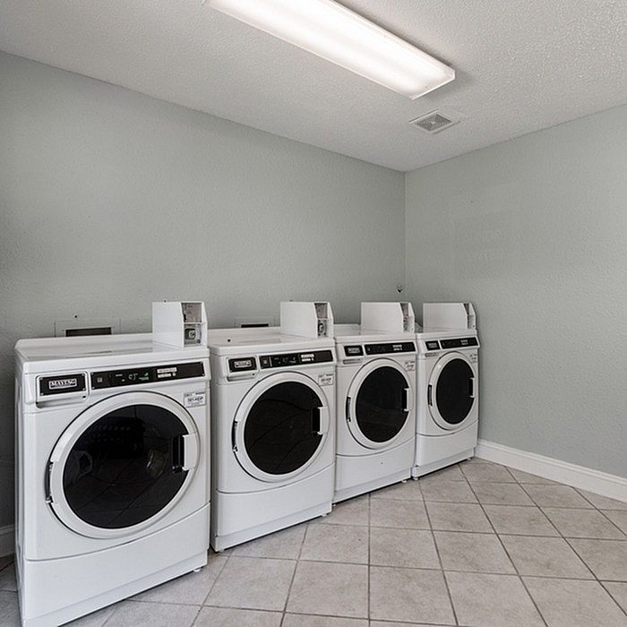 Modern laundry room with four sleek white washing machines set against a calming light grey wall, perfect for convenient living.
