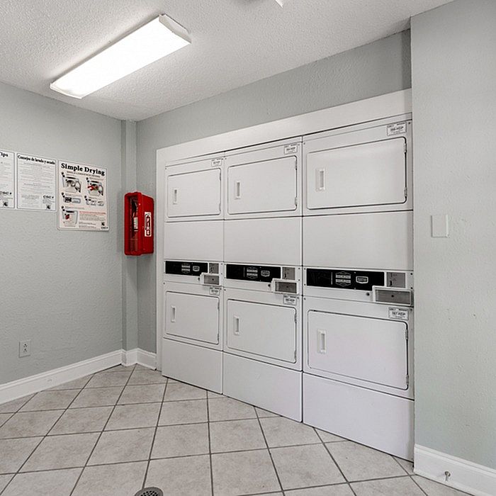 Bright and efficient laundry room with modern, stacked washers and dryers, tiled flooring, and clear usage instructions for convenience.
