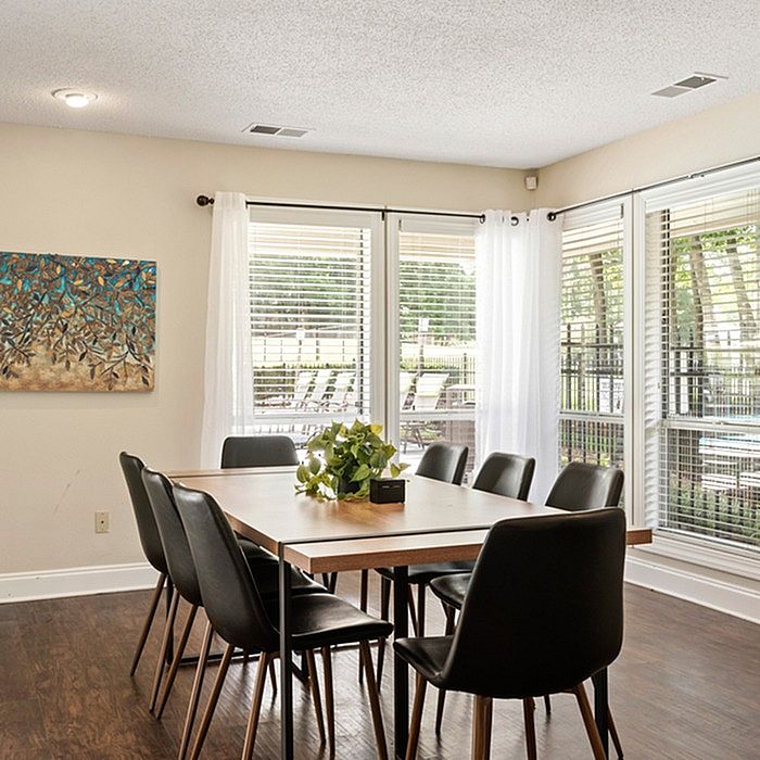 Bright dining area with elegant black chairs, modern wooden table, and large windows overlooking lush greenery.