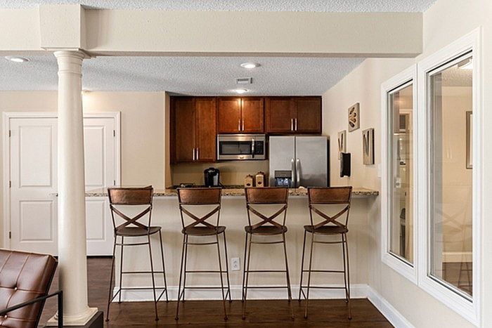 Chic apartment kitchen with modern stainless steel appliances, elegant wooden cabinetry, and a stylish breakfast bar with four high chairs.