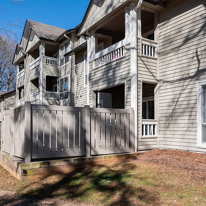 Charming multi-story apartment complex with private balconies and a cozy fenced patio, set in a serene natural environment.