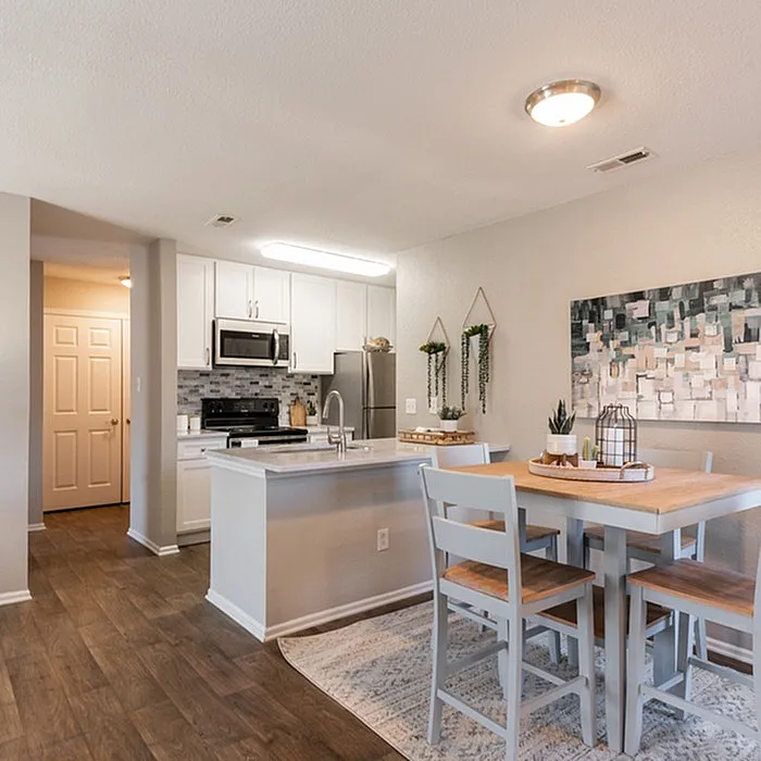 Modern kitchen and dining area with sleek white cabinetry, stainless steel appliances, and a cozy wooden dining set, perfect for entertaining.