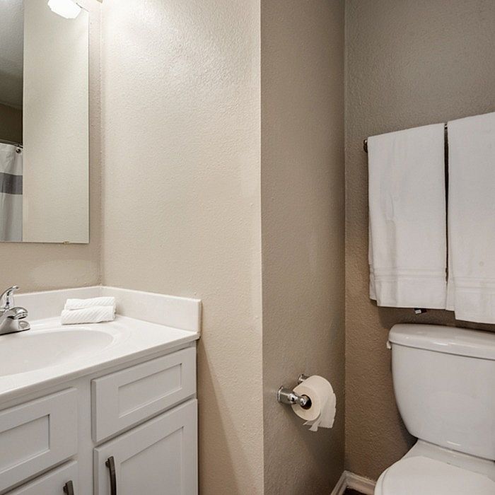 Elegant and modern bathroom featuring a sleek white vanity with a large mirror, complemented by a pristine toilet and fresh white towels.