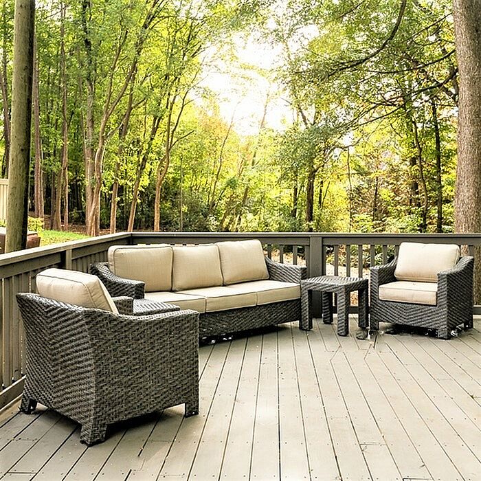 Charming outdoor patio with stylish wicker seating set, surrounded by lush green trees, offering a serene relaxation spot.