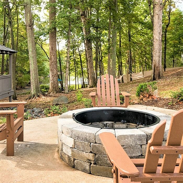 Charming outdoor fire pit area with cozy Adirondack chairs, nestled in a serene forest setting.