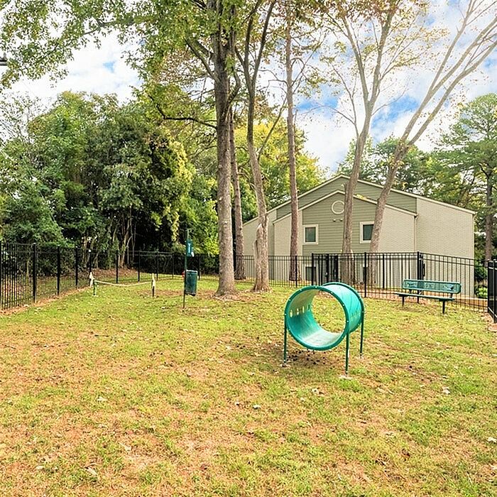 Charming fenced dog park with agility tunnel, surrounded by lush greenery near a cozy residential building.