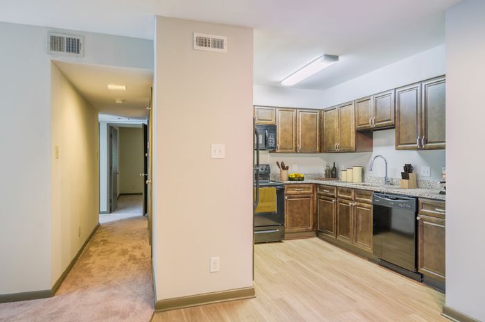 Inviting kitchen with modern wood cabinets, sleek appliances, and granite countertops next to a cozy carpeted hallway.