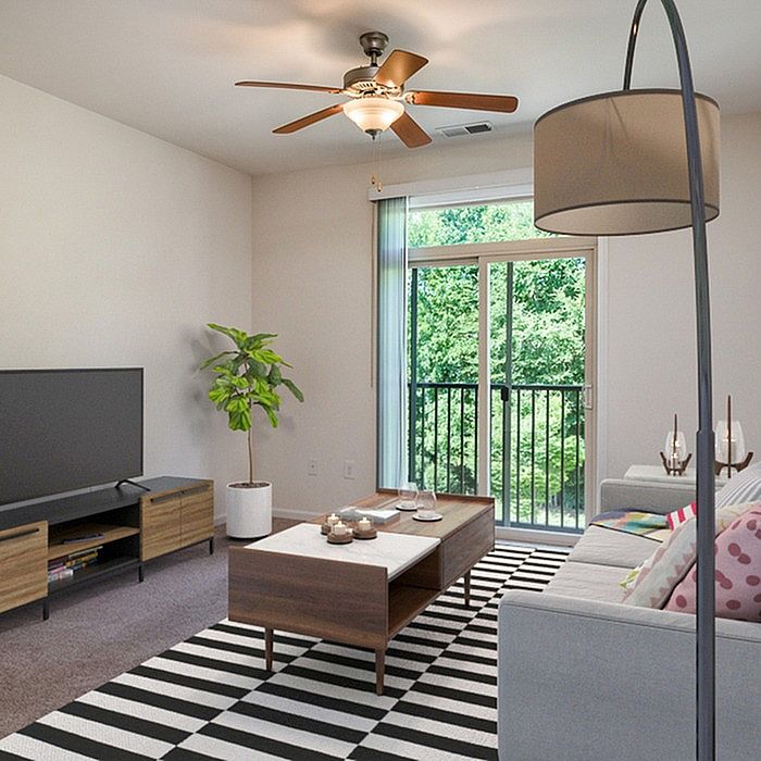 Inviting living room with modern decor, lush green view through glass doors, and cozy seating area under a stylish ceiling fan.
