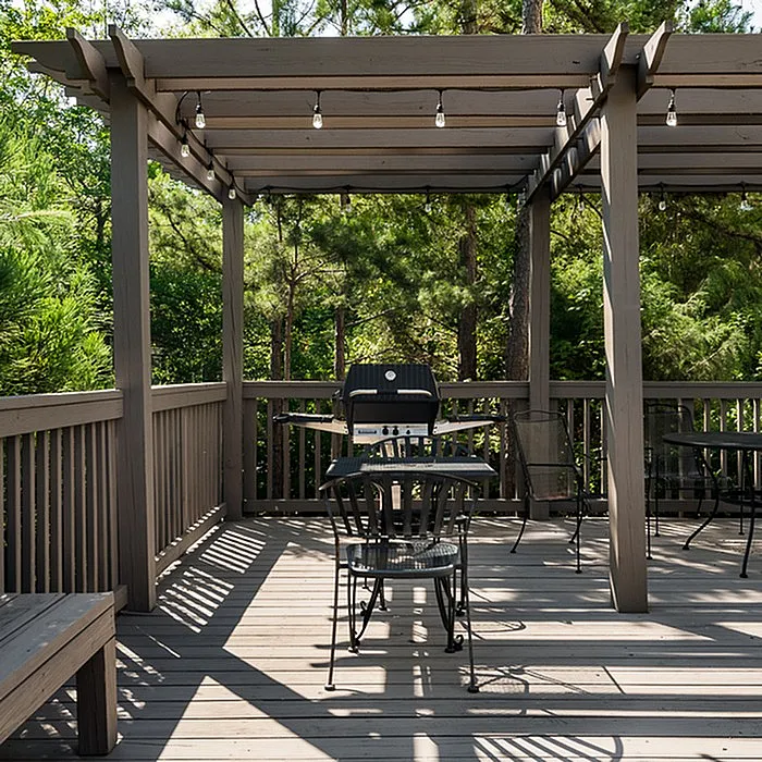 Charming outdoor deck with pergola, perfect for entertaining, featuring a sleek grill and lush greenery in the background.
