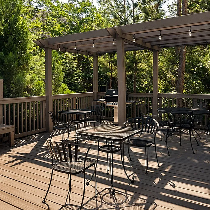 Charming outdoor patio with wooden decking and elegant iron furniture, surrounded by lush greenery and featuring a cozy pergola with string lights, perfect for entertaining.